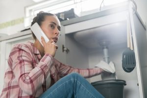 concerned-person-on-the-phone-with-leak-under-kitchen-sink